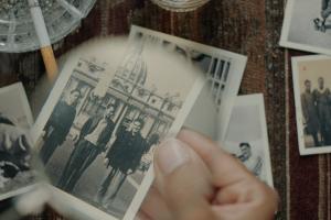 From Victoria Linares Villegas It Runs in the Family. Courtesy of True/False. Hand holding a black and white photo in focus of three people in front of a large statue and building.