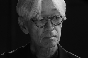 Still image from 'Ryuichi Sakamoto | Opus' depicting Sakamoto, an elderly Asian man wearing tortoiseshell glasses and with a fall of white hair over his forehead.