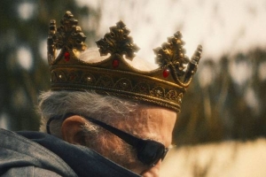 A profile view of a man wearing a crown and sunglasses.