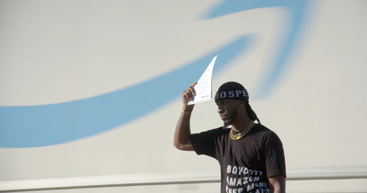 black man shades his face with a paper in front of an amazon logo