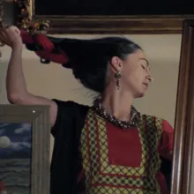 In a reflected mirror, a woman with long black hair removes a red hair ribbon.
